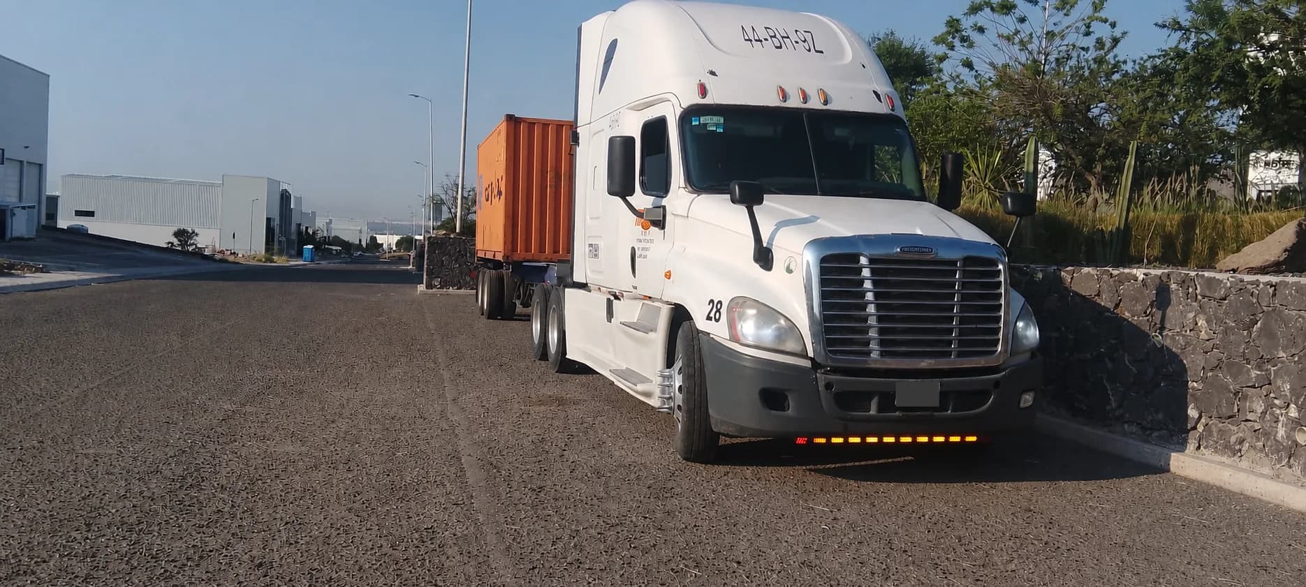 Freightliner blanco de Transportes TBP con contenedor naranja en un corredor industrial